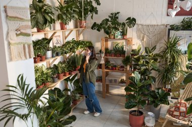 Satış elemanı, rahat bir fabrikanın raflarındaki saksı bitkilerini kontrol ediyor ve telefonla konuşuyor.