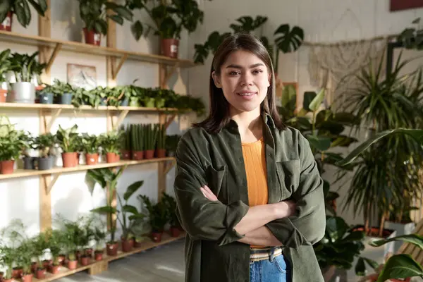 Plant store owner standing at her workplace with wide selection of potted houseplants on background