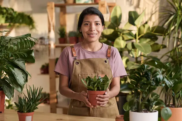 Hispanic woman posing at plant store holding pot of plant in her hands and smiling at camera