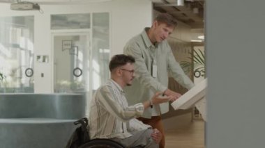 Tekerlekli sandalyedeki iş adamı ve meslektaşı interaktif dijital ekran hakkında bilgi arıyor ve modern çalışma alanında tartışıyorlar.