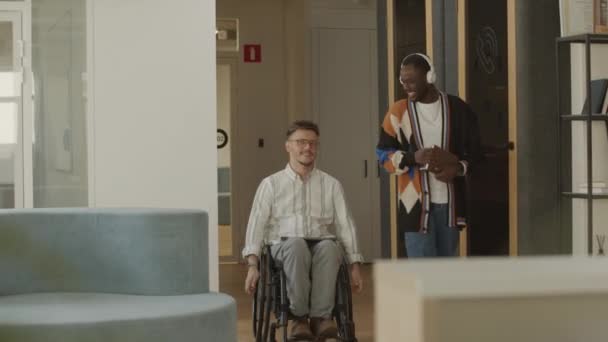 在工作日 年轻的白人商人坐着轮椅 与坐在现代办公室旁边的非裔美国男性同事聊天 — 图库视频影像