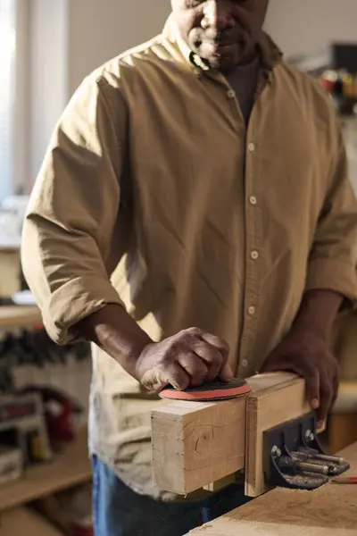 Vertical closeup of senior carpenter polishing wooden board while building furniture in workshop