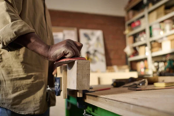 Close up of African American carpenter polishing wooden board and building furniture in workshop