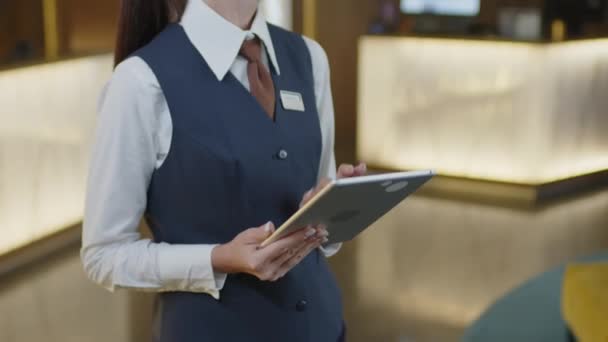 エントランスホールに立ってデジタルタブレットを使用して正式なユニフォームで女性ホテルのマネージャーのトリミングショット — ストック動画