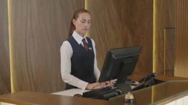 Bilgisayarda çalışan ve otelin resepsiyonundaki telefona cevap veren genç bayan hostes.