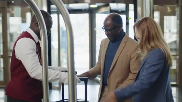 非洲裔美国人旅馆搬运工在入口大厅迎接客人 并载着装有行李箱的行李箱 — 图库视频影像