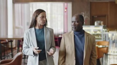 Kafkasyalı genç bir iş kadınının otel restoranında yürürken Afrika kökenli Amerikalı bir meslektaşla konuşurken orta boy fotoğrafı.