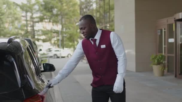 タクシータクシーのユニフォームオープンドアとホテルに到着する女性ゲストを迎える若いアフリカ系アメリカ人ポーター — ストック動画