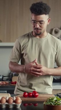 Genç yemek blogcusunun kameraya bakıp mutfak masasındaki malzemeleri tarif ederken çevrimiçi aşçılık dersi verirken ya da yemek programını çekerken dikey görüntüsü.