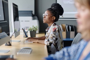 Genç Afrikalı Amerikalı programcı ofisteki masaüstü bilgisayarında veri ile çalışıyor.