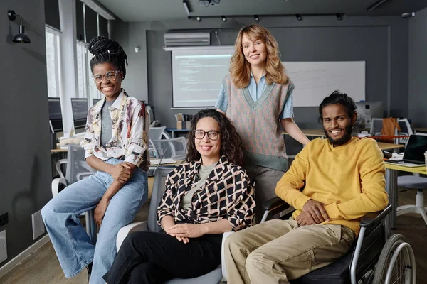 Diverse group of young coworkers posing together in office sitting and smiling at camera