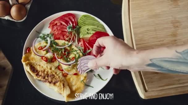 プレート上の野菜やハーブとオムレツを提供するシェフのトップダウンショット ビデオレシピ中に下の画面に表示される字幕 — ストック動画