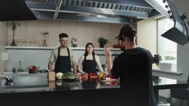 Genç erkek ve kadın aşçıların sunduğu yemek programının kameramanı mutfak masasının yanında yemek malzemeleriyle yemek tarifi veriyor.