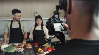 Kameramanların, mutfak masasının arkasında durup yemek malzemelerini anlatan iki genç aşçıyı kameraya çekerken ve TV 'de yemek programı sunarken...