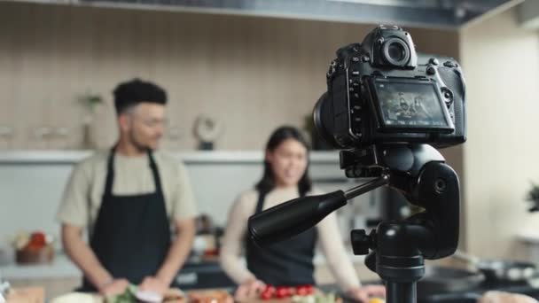 キッチンの若いフードブロガーが主催する三脚撮影料理ショーに設定されたデジタルカメラの選択的なフォーカスショット — ストック動画