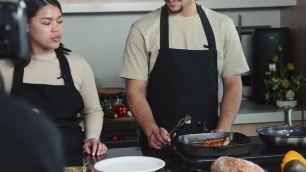 キッチンで料理番組を撮影しながら シェフと彼の女性の共同ホストの撮影とカメラの前でステーキを調理 — ストック動画