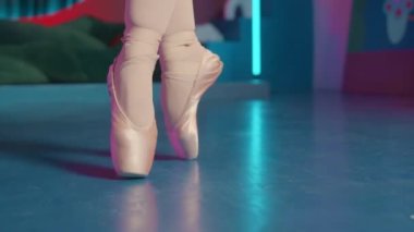 Bale ayakkabılı balerin bacaklarının yakın plan çekimi sahnede neon ışıkla dans ediyor.