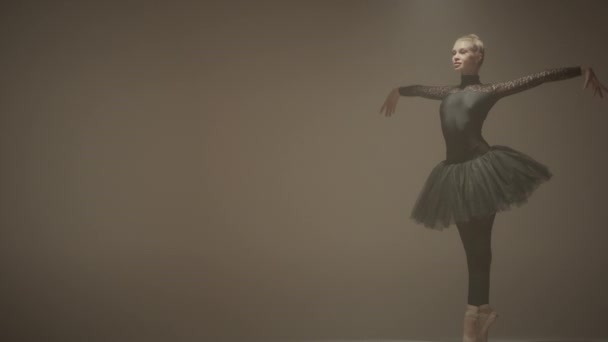 ブラックチュウで美しいバレリーナのスタジオショットとアラベスクを実行し サイクルの壁の背景に踊るポントシューズ — ストック動画