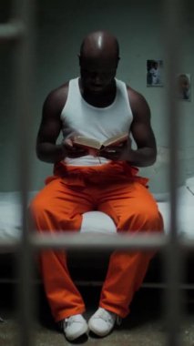 Hapisteki hücrede oturmuş, İncil okuyup dua eden siyah mahkûmlardan oluşan duvardan dikey bir atış.