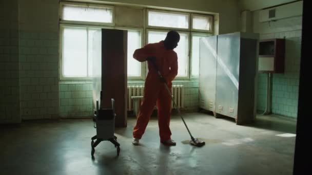 オレンジ色の均一なモッピングフロアでアフリカ系アメリカ人の男性囚人の完全なショット — ストック動画
