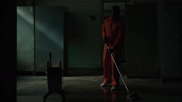 穿着监狱制服的男囚犯在黑暗房间用拖把清扫地板 同时履行职责 — 图库视频影像