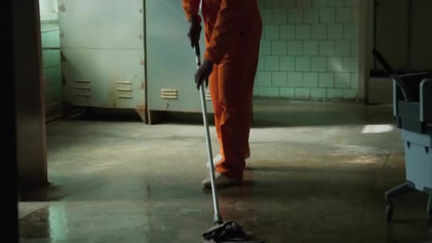 Наклоните Снимок Чернокожего Заключенного Оранжевом Комбинезоне Вытирающего Пол Тюремной Комнате — стоковое видео