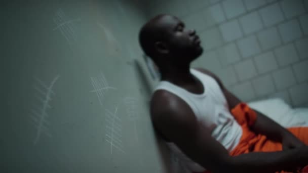 Rack Focus Shot Tired Czarny Więzień Siedzi Łóżku Więziennej Celi — Wideo stockowe