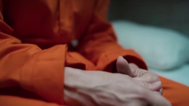 暗い刑務所のセルに座っているオレンジ色の制服で神経質な女性の囚人の近くの傾きのショット — ストック動画