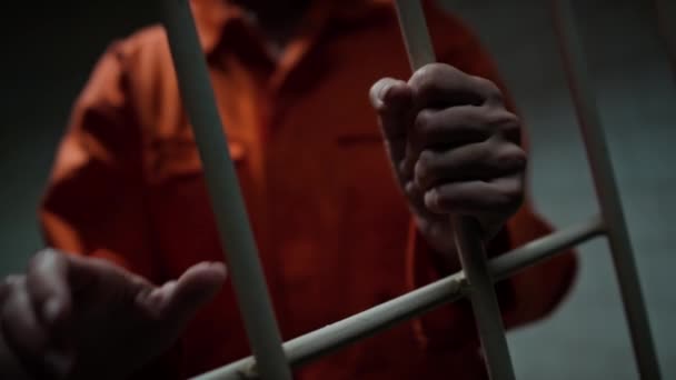 刑務所の刑務所のバーを保持するオレンジの制服で認識できない囚人の手の閉鎖ショット — ストック動画