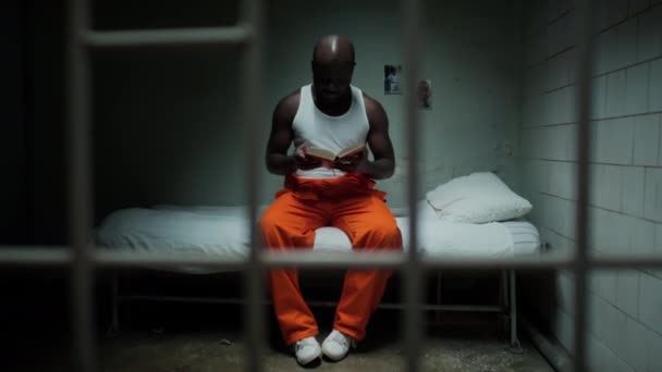 Blick Durch Gitter Afroamerikaner Sitzt Auf Bett Gefängniszelle Liest Bibel — Stockvideo