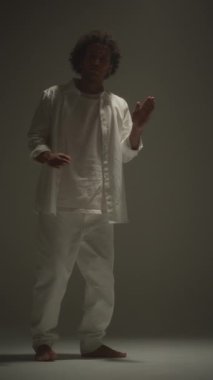 Beyaz takım elbiseli genç bir adamın dikey olarak stüdyoda robot dansı yaptığı sahne.