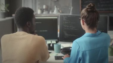 Genç siyahi bir adam ve beyaz bir kadının bilgisayar başında oturmuş bilişim projesinde çalışırken çift ekran programlama kodlarını tartışırken...