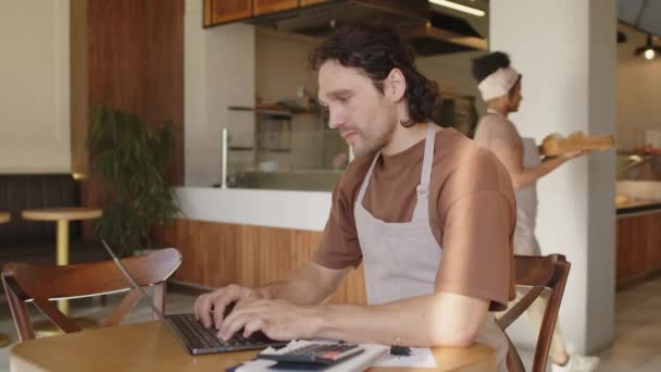 Чоловік Власник Пекарні Фартусі Використовує Ноутбук Перевіряє Квитанції Під Час — стокове відео