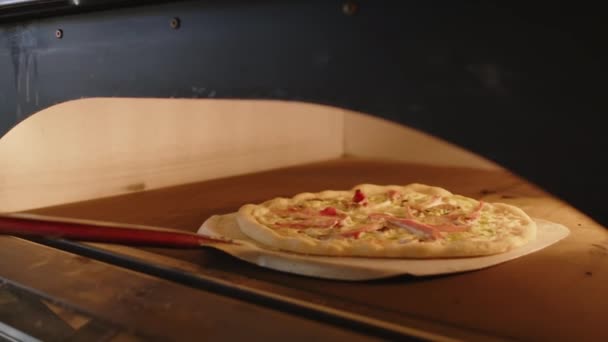 ピザ屋のキッチンで食べ物を調理しながら 熱いオーブンやクローズドアから皮に焼いたおいしいピザを除去する認識できないシェフの近いビュー — ストック動画