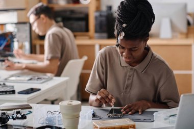 Siyah teknisyen bozuk telefonu tornavidayla tamir ediyor. Erkek arkadaşı da arka plan üzerinde çalışıyor.