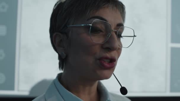 有经验的女医生 身穿白衣 戴着眼镜 在投影屏前用麦克风交谈 并在医护会议上作报告 — 图库视频影像