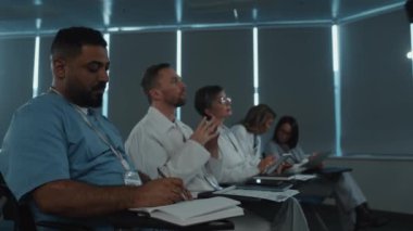 Profesyonel doktorlar konferans salonunda oturup hoparlörleri dinliyor ve tıp semineri sırasında notlar alıyorlar.