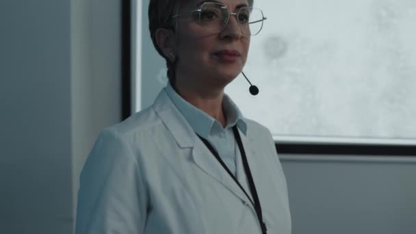 Beyaz Önlük Mikrofon Takan Kadın Doktor Projeksiyon Ekranının Önünde Yürüyor — Stok video