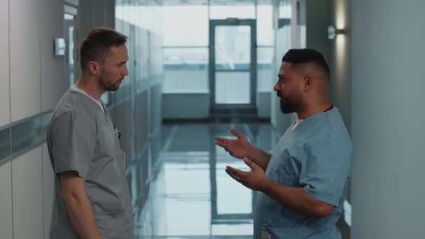 医療ユニフォームの男性2人の病院労働者が話し 握手し 廊下を歩いている — ストック動画