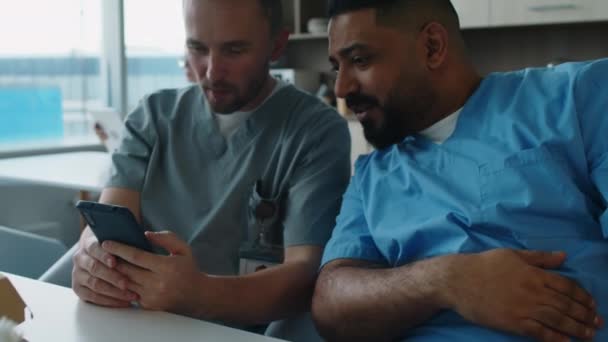 两名男性医务工作者坐在休息室的灌木丛中 一边打电话一边在网上聊天 一边吃午饭 他们的照片被放大了 — 图库视频影像