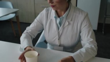 Hastanedeki iş günlerinde baş ağrısı hissederken orta yaşlı kadın doktorların ilaç içip, su içerek ve dinlenme odasında alnını ovalayarak fotoğraf çektiririz.