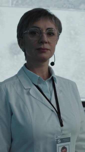 医疗会议期间 中年妇女医生头戴话筒耳机 头戴白色外套 戴着眼镜 在投影屏幕前摆姿势拍照的垂直肖像 — 图库视频影像