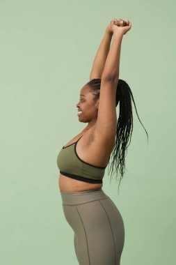 Dikey yan görüntü stüdyosu, neşeli, Afro-Amerikan bir kadının spor kıyafetleri içinde kendini esnetirkenki görüntüleri.
