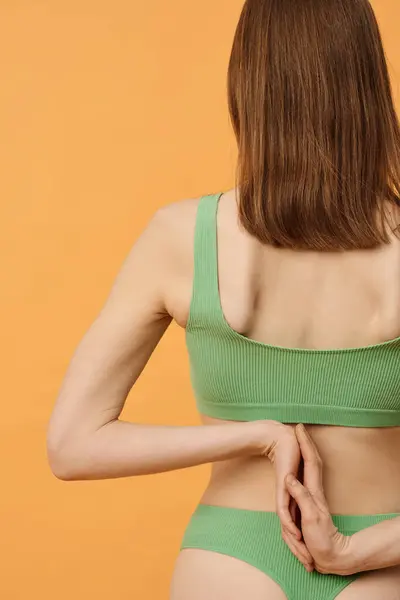 Rear view studio shot of unrecognizable Caucasian woman with brown hair wearing pale green underwear posing for camera with hands behind her back