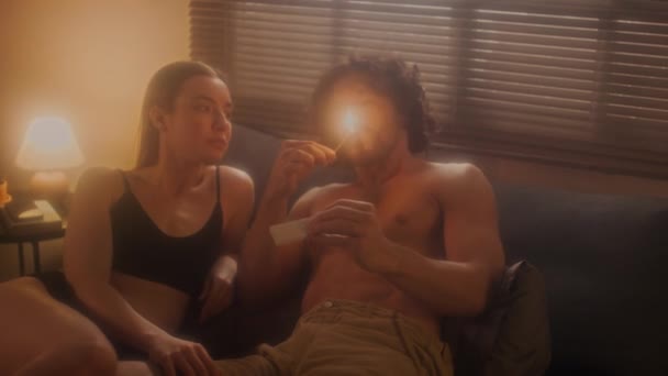 若いシャツレスの男は ベッドルームでロマンチックな夜の間に愛するガールフレンドとタバコを点灯し 喫煙し カドリング — ストック動画