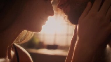 Birbirlerine aşık genç bir çiftin yatak odasının penceresinden süzülen sıcak ışığa karşı öpüştüğü yakın çekim.