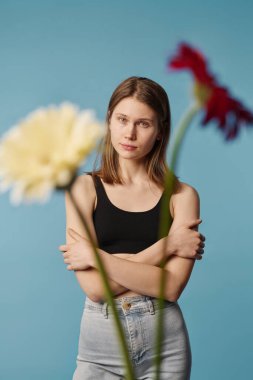 İki Gerbera çiçeğinin önünde kollarını kavuşturup kameraya bakarken seçici bir odak fotoğrafı.