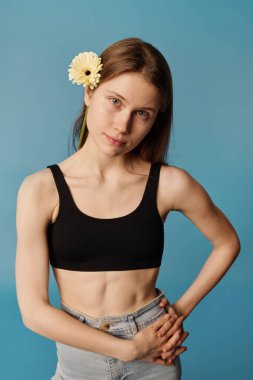 Dikey orta stüdyo portresi. Kırpılmış bluz giyen genç bir kadın. Saçında kot pantolon ve çiçek var.