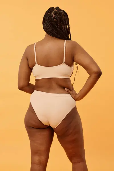 Vertical medium long back view shot of unrecognizable Black woman with curvy body wearing minimalistic lingerie posing for camera in studio