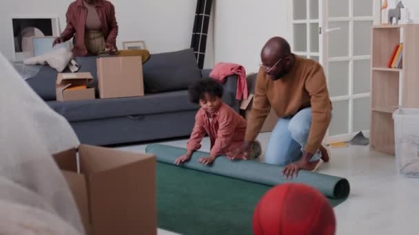 アフリカ系アメリカ人の父親と小さな息子がカーペットを転がし 母親がバックグラウンドで荷物を詰めながら お互いに高い5を与える — ストック動画